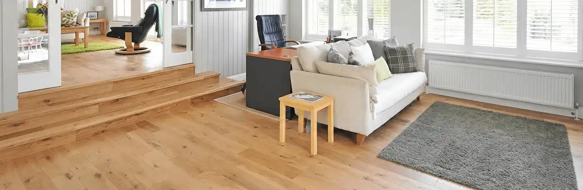 A modern living room with professionally installed laminate flooring, a beige sofa, a small side table, a gray rug, and large windows with white shutters in Pittsburgh, PA